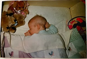 baby sleeping in a crib with a rainbow quilt to keep warm
